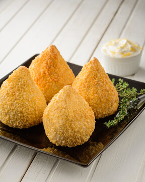 Four crispy delicious brazilian coxinhas or drumsticks on a black square plate with white wood table background