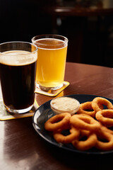 Crispy, golden onion rings sprinkled with sea salt in a bowl And beer glasses on a wooden table.