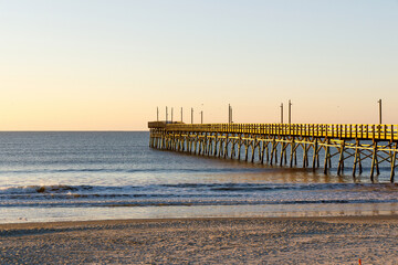 Fishing pier on the Atlantic Ocean at sunrise in Sunset Beach, North Carolina.  Clear sky and calm seas.