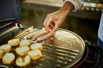 Fototapeta Close up on man's hand put sausages and roasting bruschetta on the barbecue gas grill obraz