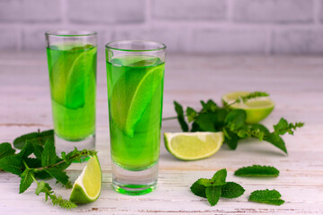 Delicious mint liqueur with lime and mint leaves on a white wooden table.
