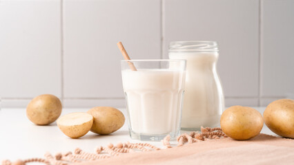 A glass and bottle with potato milk on the table with the potato tubers. Vegan trend in healthy eating. Alternative plant milk