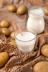 Obraz na płótnie Canvas A glass and bottle with potato milk with the potato tubers. Vegan trend in healthy eating. Alternative plant milk