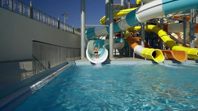 Happy woman cheering as she exits a water slide into a pool