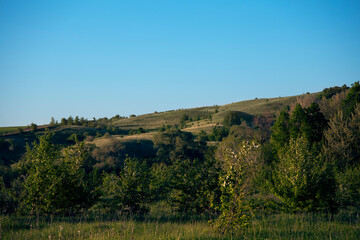 Beautiful landscape on a sunny day. An earthen road. A landscape with a colorful sky under the sun. Mountain slope. Green trees.against the background of a green forest clearing.summer meadow