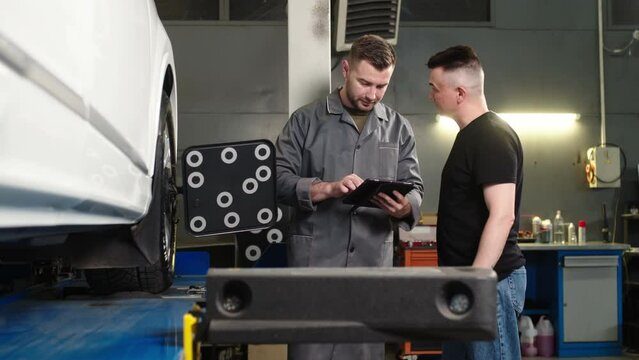 mechanic and service manager in a repair shop near a car diagnosing and checking a car together in a car service, using a tablet and discussing repairs