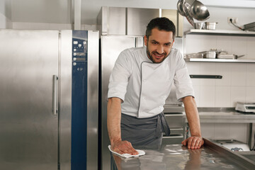 Young handsome male chef cleaning his workplace on kitchen in restaurant