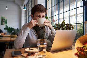 Woman working on a notebook and drinking coffee at a table in a cafe