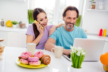 Photo of excited pretty age boyfriend girlfriend wear t-shirts talking modern gadgets enjoying breakfast indoors room home