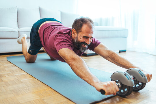 Positive athletic bearded middle-aged man exercising at home, using laptop, watching sport videos on Internet, having fitness class online, copy space. Healthy lifestyle, sport on self-isolation