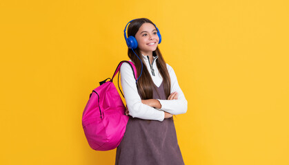 cheerful child in headphones with school backpack on yellow background