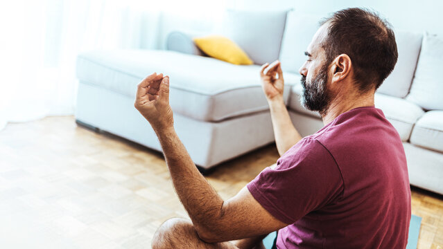 Mature Adult Man Meditating in His Living Room Floor Sitting in the Lotus Position With His Eyes Closed and an Expression of Tranquility in a Health and Fitness Concept. Mature man meditating at home