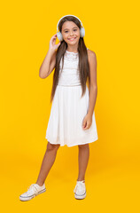 positive teen girl listen music in headphones on yellow background