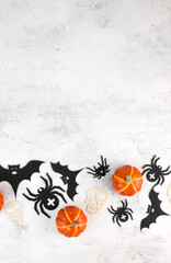 Obraz na płótnie Canvas Vertical halloween background with skulls,pumpkins,bats abd spiders on white concrete. Invitation or card for october 31.Copy space