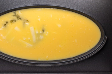 オムレツクッカーに入れた溶き卵およびチーズ
