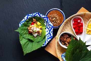 Fototapeta na wymiar Thai Food concept Fusion Thai snack Miang kham herbal and tuna one bite wrap by perilla leave(shiso) with blend herbals coconut sugar sauce on black background with copy space
