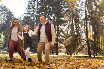 Senior couple with granddaughter walking at the park during the autumn