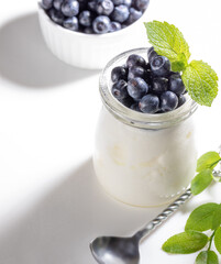 Natural yogurt in glass jar with fresh forest blueberries on white background. Copy space.