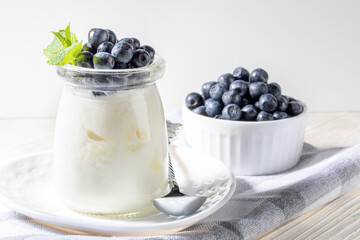 Natural homemade yogurt in glass jar with fresh forest blueberries on kitchen napkin on white.
