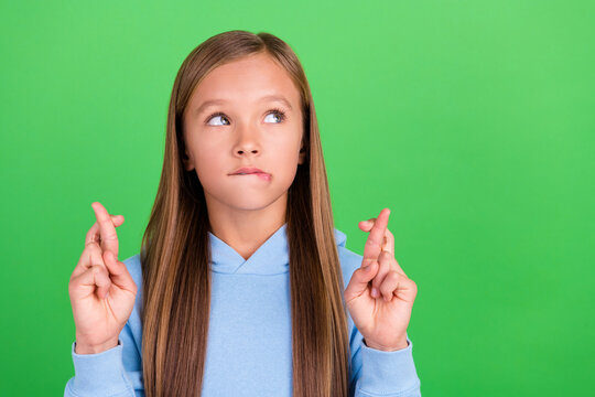 Close up photo of funky small girl fingers crossed worry exam results dressed stylish blue sweatshirt isolated on green color background
