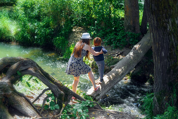 a woman in a dress and a little boy are walking in nature. Forest river. A log across the stream.