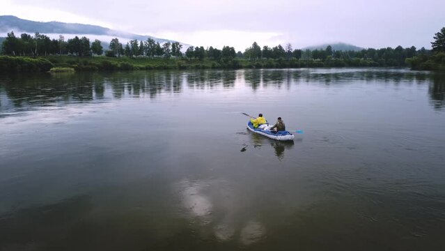 Two men are rafting on a calm river on an inflatable kayak on the Siberian river in summer. Active weekend in the wild