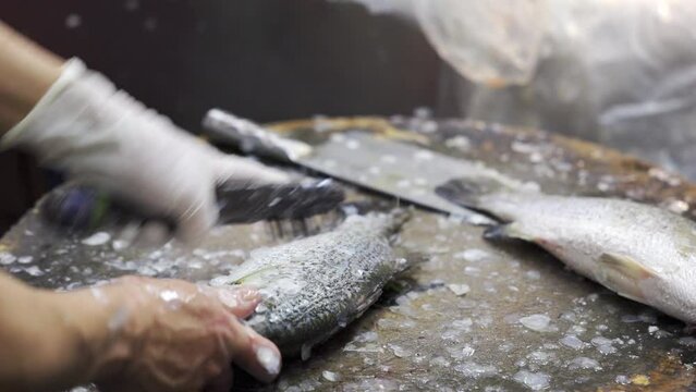 A fishmonger removing fish scales using fish scalier on Chopping board preparing fresh fishes for his customer at fresh market.
