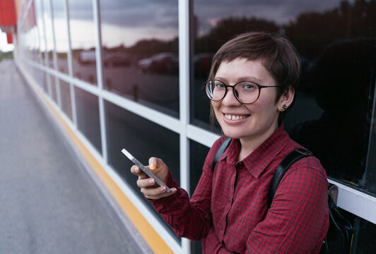 Beautiful young girl in glasses on the street with a phone in his hand , smiling and looking at the camera . Against the background of the city perspectives .