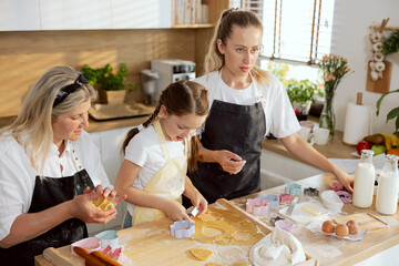 Happy family time in kitchen. Granny kneading dough in hands young mother looking at husband...