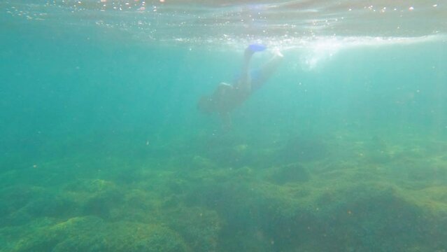 Underwater footage scene of young man snorkeling, swimming with fins, searching and hunting fish with spear in the sea. Turquoise color of the water. Summer holidays activity.	