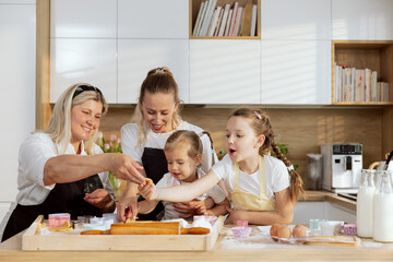 Christmas time. Family spending time in modern light kitchen preparing cookies for baking. Grandmother and young mother teaching offsprings baking cooking christmas cookies biscuits preparing surprise