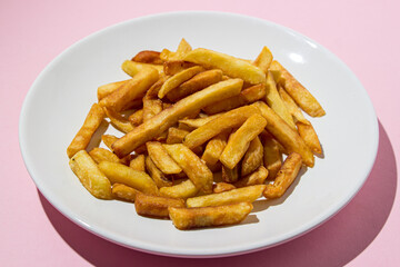 French fries on a white plate on a pink background. A delicious way to cook potatoes. Delicious fast food