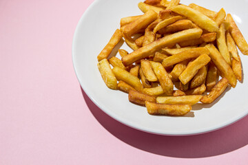 French fries on a white plate on a pink background. A delicious way to cook potatoes. Delicious fast food