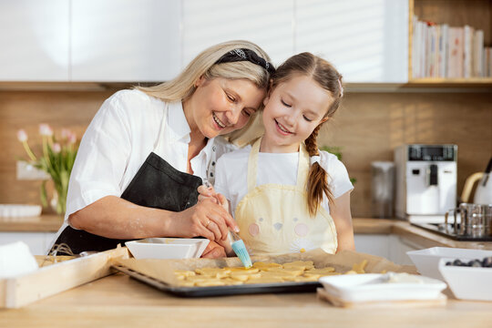Happy delighted mother with young schooler daughter in the kitchen spending time together baking cooking preparing cookies for putting in oven. Beautiful happy girl having fun at the weekend.