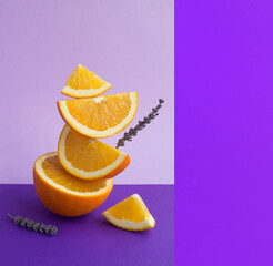 Fototapeta Orange fruit and lavender flower stacked pyramid on the purple background. Copy space. obraz