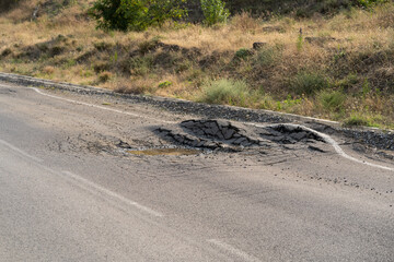 Fototapeta Deep hole in the road. Deformed asphalt surface with potholes melts from heat due to heavy overloaded trucks driving at hot summer days.  obraz