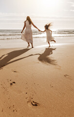 Anonymous mother with daughter holding hands and running on sandy seashore