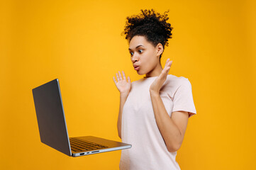 Emotional puzzled shocked curly haired african american young woman, looks in surprise at the...
