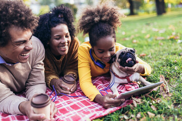 Beautiful young family lying on a picnic blanket with their dog, enjoying an autumn day in park...