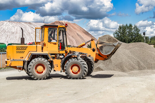 A large front loader transports crushed stone or gravel in a bucket at a construction site or concrete plant. Transportation of bulk materials. Construction equipment. Bulk cargo transportation.