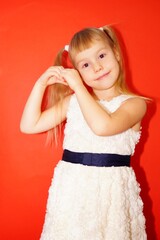 Idea of new year. Little girl with white dress on red background. Palms are folded in the shape of heart.