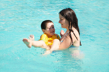 Fototapeta na wymiar Mother and son swim in the pool, the child learns to swim in an inflatable vest