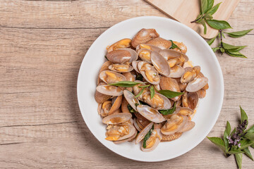 Stir fried clams with basil leaves in a white bowl