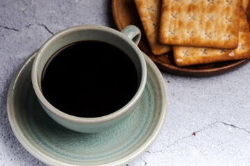 Hot black coffee in a green coffee cup with crackers.