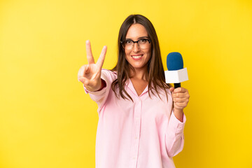 hispanic young adult woman smiling and looking happy, gesturing victory or peace. interviewer with...