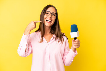hispanic young adult woman smiling confidently pointing to own broad smile. interviewer with a...