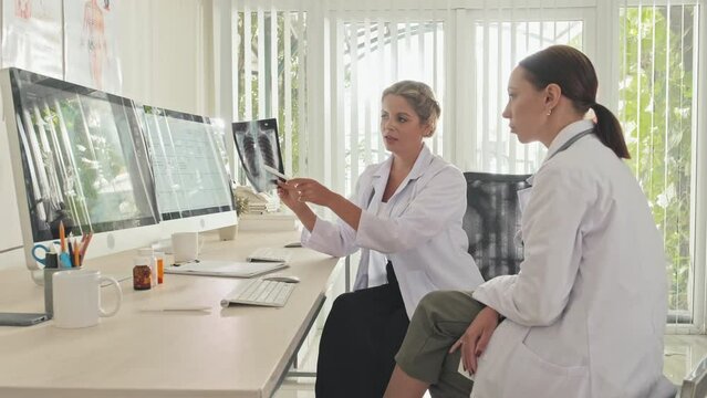 Two female doctors discussing chest x ray scan while cooperating during workday in clinic