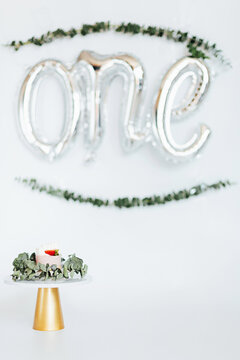 Beautiful photo session set up for baby girl celebrating one year old birthday on white background. Delicious biscuit cake with butter cream and candle one
