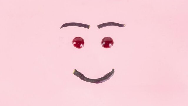 4k Smiley face made from purple asparagus beans, cherries and blueberries moves and talks, moves its eyes and blinks. Concept of berries season and proper nutrition. Pink background. Stop motion anima