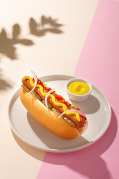Hot dog in a round plate on white and pink background